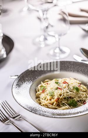 Italienische Spaghetti Algio e Olio mit Knoblauch-Parmesan und Chili-Paprika auf festlichem Tisch im Restaurant. Stockfoto