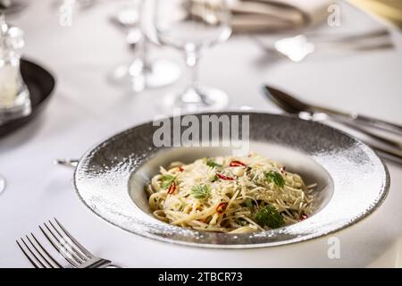 Italienische Spaghetti Algio e Olio mit Knoblauch-Parmesan und Chili-Paprika auf festlichem Tisch im Restaurant. Stockfoto