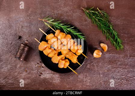 Rohe Hähnchenspieße in Marinade mit Gewürzen auf einem schwarzen Teller und auf einem braunen Tisch Stockfoto