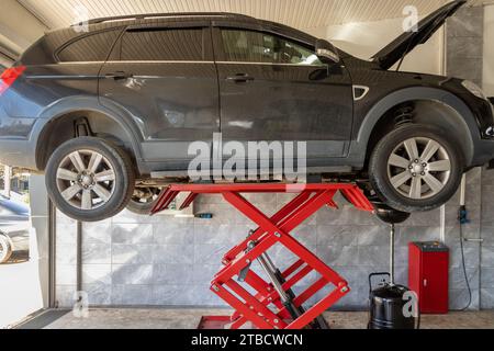 Das Fahrzeug, dessen Reparatur an der Tankstelle abgeschlossen ist, wird vom Aufzug abgenommen. Arbeitsbereich mit Fahrzeug auf Hochaufzug in der Fahrzeugreparaturwerkstatt Stockfoto