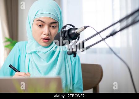 Muslimische Frau mit Hijab und Kopfhörern, die zu Hause Hörbücher und Podcasts hört, zufriedene und erfolgreiche Frau. Stockfoto