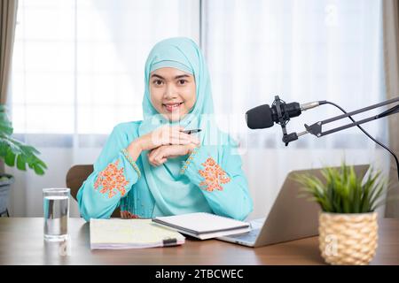 Muslimische Frau mit Hijab und Kopfhörern, die zu Hause Hörbücher und Podcasts hört, zufriedene und erfolgreiche Frau. Stockfoto