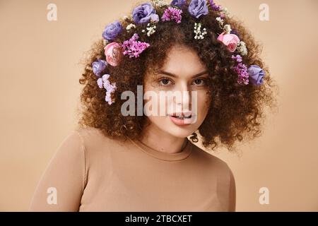 Porträt einer glücklichen Frau mit bunten Blumen im Haar lächelnd in die Kamera auf beige, natürliche Schönheit Stockfoto