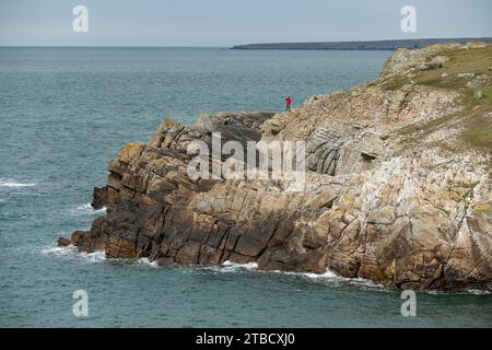 Man stand auf Klippen an der felsigen Küste nahe Rhocolyn am Wales Coast Path in Anglesey, Nordwales Stockfoto