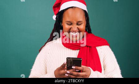 Die junge schwarze Frau im Weihnachtsmann-Hut lächelt, schickt Freunde über Weihnachten, im Studio Stockfoto
