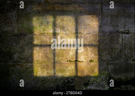 Sanftes Licht, das durch einen Fensterrahmen auf eine alte Steinmauer mit Moos leuchtet Stockfoto