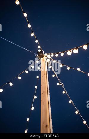 Dekorative Lichterketten hängen an einer Holzstange. Wolframlampen, dunkelblauer Himmel, niedriger Blickwinkel, keine Leute. Stockfoto