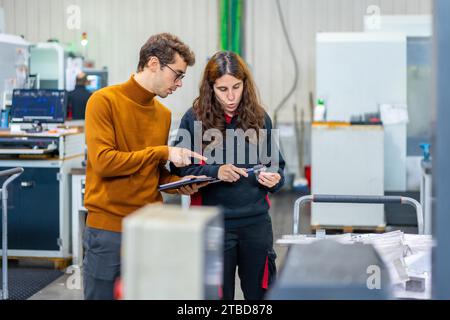 Qualitätskontrolle von zwei Ingenieuren, die stehen und sprechen, während sie ein Tablet in einer cnc-Fabrik verwenden Stockfoto