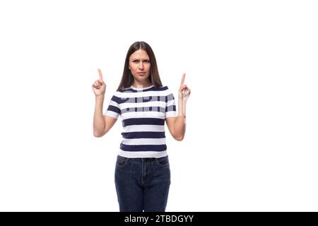 Eine junge europäische Dame mit schwarzen, gleichmäßigen Haaren in einem gestreiften T-Shirt zeigt mit ihrem Zeigefinger auf Ideen und Nachrichten Stockfoto