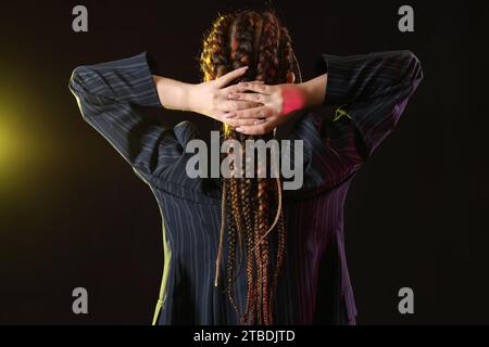 Junge Frau mit Dreadlocks auf dunklem Hintergrund, Rückansicht Stockfoto