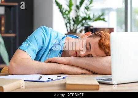 Müder männlicher Medizinstudent, der am Tisch in der Bibliothek schläft Stockfoto