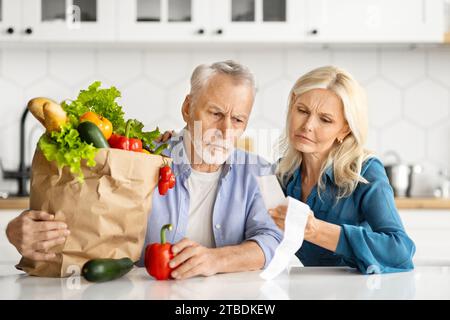 Besorgtes Seniorenpaar, das nach dem Einkaufen lange Lebensmittelbelege genau überprüft Stockfoto