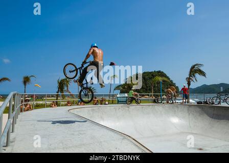 Santos City, Brasilien. BMX-Radfahrer, der im Skatepark Emissário Tricks in der Luft vorführt. Im Hintergrund die Insel Urubuqueca und der Strand Stockfoto