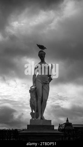 Eine Bronzestatue einer männlichen Figur mit einem Vogel auf dem Kopf, umgeben von einer üppigen grünen Landschaft Stockfoto