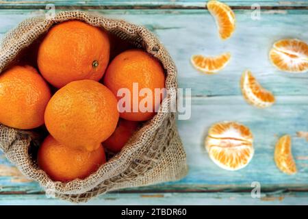 Blick von oben auf Mandarinen in Jutebeutel auf alten türkisfarbenen Holztisch mit geschälten Mandarinenstücken, gesunde reife Zitrusfrüchte in einem Jutebeutel Stockfoto