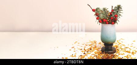 Banner mit einem Blumenstrauß aus Nobilis Tanne und Winterbeerzweigen und goldfarbenem Konfetti vor beigem Hintergrund. Stockfoto