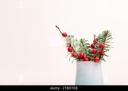 Strauß aus Edeltanne und Winterbeerzweigen in einer Vintage-Vase vor beigem Hintergrund. Festliche Komposition mit Platz für Text. Stockfoto