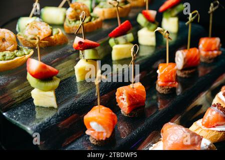 Verschiedene Gourmet-Canapes mit frischen Belägen auf einem reflektierenden schwarzen Serviertablett für gehobene Veranstaltungen. Stockfoto