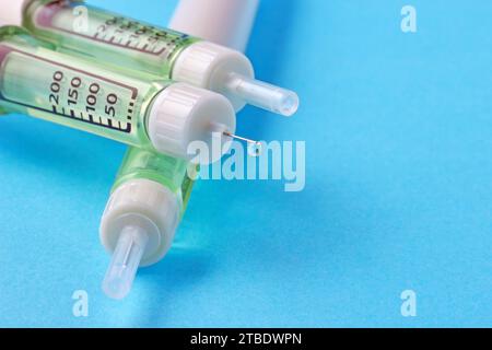 Insulinspritzenpen mit einem Tropfen Insulin am Ende der Nadel auf blauem Hintergrund. Stockfoto