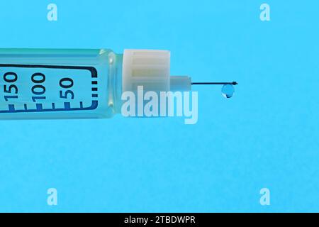 Insulinspritze mit einem Tropfen Insulin am Ende der Nadel auf blauem Hintergrund mit Kopierraum. Stockfoto