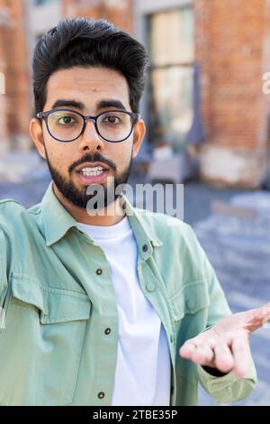 Ein junger Indianer hat auf der Straße einen Videoanruf am Telefon, Gesten und Blick in die Kamera. Stockfoto