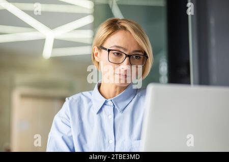 Porträt einer konzentrierten seriösen, gut gekleideten Büroangestellten, die einen Computer in einem hellen modernen Büro benutzt. Stockfoto