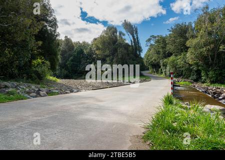 Fahrzeughintergrund oder Rückwand mit einer Landstraße mit einer niedrigen Brücke, die über einen Fluss oder Fluss führt Stockfoto