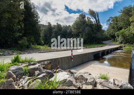 Fahrzeughintergrund oder Rückwand mit einer Landstraße mit einer niedrigen Brücke, die über einen Fluss oder Fluss führt Stockfoto