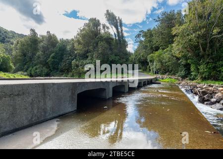 Fahrzeughintergrund oder Rückwand mit einer Landstraße mit einer niedrigen Brücke, die über einen Fluss oder Fluss führt Stockfoto