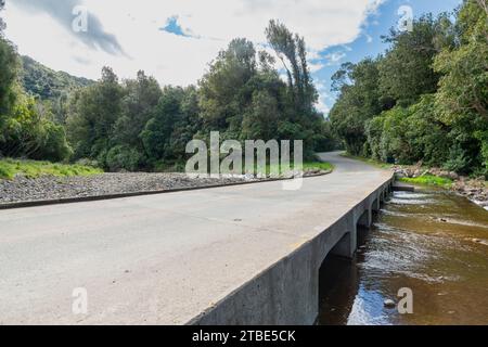 Fahrzeughintergrund oder Rückwand mit einer Landstraße mit einer niedrigen Brücke, die über einen Fluss oder Fluss führt Stockfoto