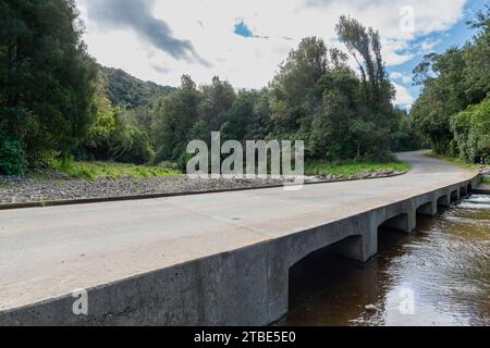 Fahrzeughintergrund oder Rückwand mit einer Landstraße mit einer niedrigen Brücke, die über einen Fluss oder Fluss führt Stockfoto