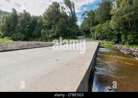 Fahrzeughintergrund oder Rückwand mit einer Landstraße mit einer niedrigen Brücke, die über einen Fluss oder Fluss führt Stockfoto