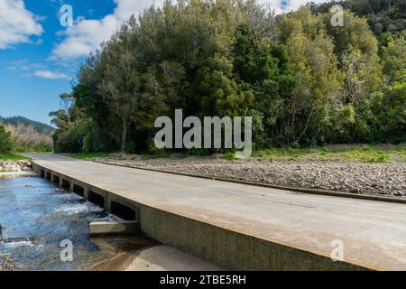 Fahrzeughintergrund oder Rückwand mit einer Landstraße mit einer niedrigen Brücke, die über einen Fluss oder Fluss führt Stockfoto