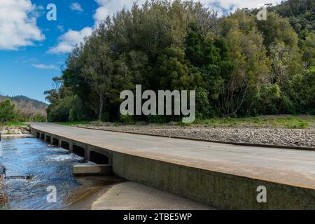 Fahrzeughintergrund oder Rückwand mit einer Landstraße mit einer niedrigen Brücke, die über einen Fluss oder Fluss führt Stockfoto