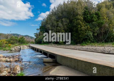 Fahrzeughintergrund oder Rückwand mit einer Landstraße mit einer niedrigen Brücke, die über einen Fluss oder Fluss führt Stockfoto