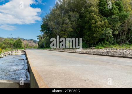 Fahrzeughintergrund oder Rückwand mit einer Landstraße mit einer niedrigen Brücke, die über einen Fluss oder Fluss führt Stockfoto