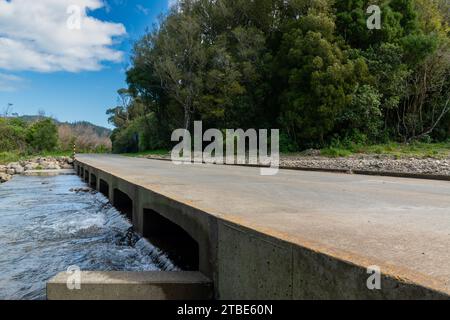 Fahrzeughintergrund oder Rückwand mit einer Landstraße mit einer niedrigen Brücke, die über einen Fluss oder Fluss führt Stockfoto