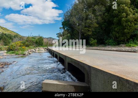 Fahrzeughintergrund oder Rückwand mit einer Landstraße mit einer niedrigen Brücke, die über einen Fluss oder Fluss führt Stockfoto