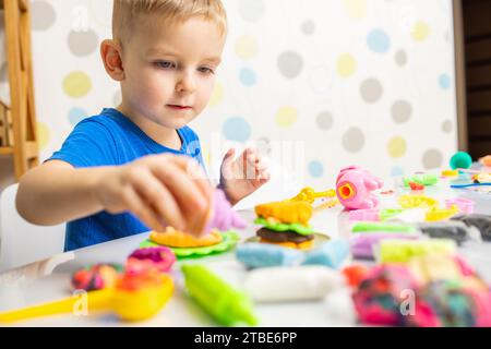 Der kleine Junge spielt begeistert mit Plastilin, spielt Teig auf weißem Tisch Stockfoto