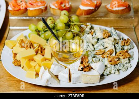 Elegante Käseauswahl mit Brie, Blauschimmelkäse und Cheddar, serviert mit Honig, Walnüssen, und grüne Trauben. Stockfoto