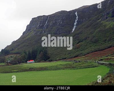 Insellandschaft mit hohen Klippen und stürzenden windgepeitschten Wasserfällen über einem traditionellen roten Haus am Straßenrand in Ross of Mull, Mull, Schottland, Großbritannien Stockfoto