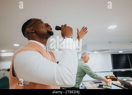 Gutaussehender männlicher Angestellter singt im Büro, während er Nachtschicht arbeitet. Die Arbeit läuft gut, er ist glücklich, positiv und zufrieden. Stockfoto