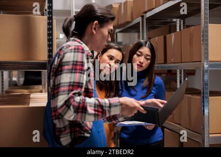 Lagerpersonal, das die Paketlogistik und -Verteilung im Lagerraum verwaltet. Storehouse asiatisches Team für Männer und Frauen überprüft gemeinsam den Bericht zur Produktqualitätskontrolle auf einem Laptop Stockfoto