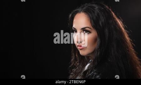 Junge selbstbewusste Frau in einer schwarzen Studioumgebung Stockfoto