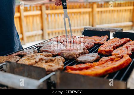 BBQ Picknick draußen. Gegrillter Schweinebauch in Marinade. Fleisch dreht sich auf dem Grill. Appetitliches gebratenes Schweinefleisch. BBQ und Grill. Gegrilltes Fleisch. Picknick im Freien Stockfoto