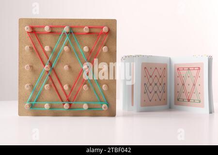 Geoboard aus Holz mit Gummibändern und Anleitung auf weißem Tisch. Lernspielzeug für die motorische Entwicklung Stockfoto