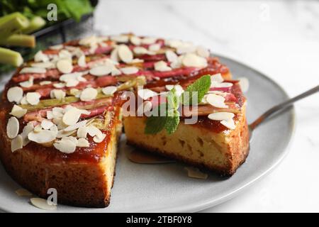 Frisch gebackener Rhabarberkuchen mit Mandelflocken und Tortenheber auf weißem Tisch, Nahaufnahme Stockfoto