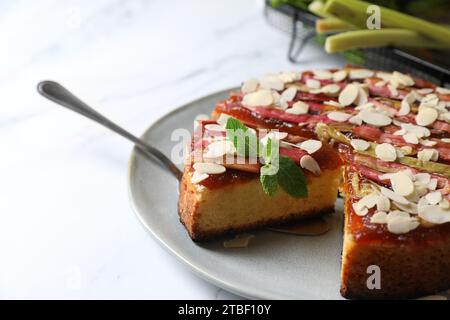 Frisch gebackener Rhabarberkuchen mit Mandelflocken und Tortenheber auf weißem Marmortisch, Nahaufnahme Stockfoto