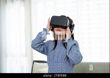 Ein süßes und aufgeregtes junges asiatisches Mädchen trägt ein VR-Headset und erlebt zu Hause ein Virtual-Reality-Spiel. Virtual-Reality-Gaming Stockfoto