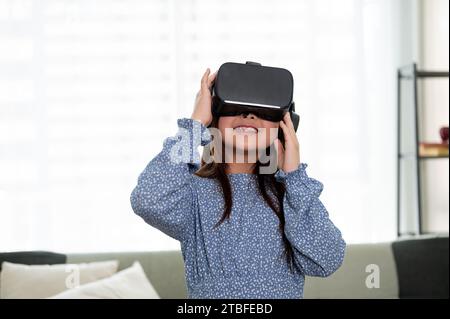 Ein süßes und aufgeregtes junges asiatisches Mädchen trägt ein VR-Headset und erlebt zu Hause ein Virtual-Reality-Spiel. Virtual-Reality-Gaming Stockfoto